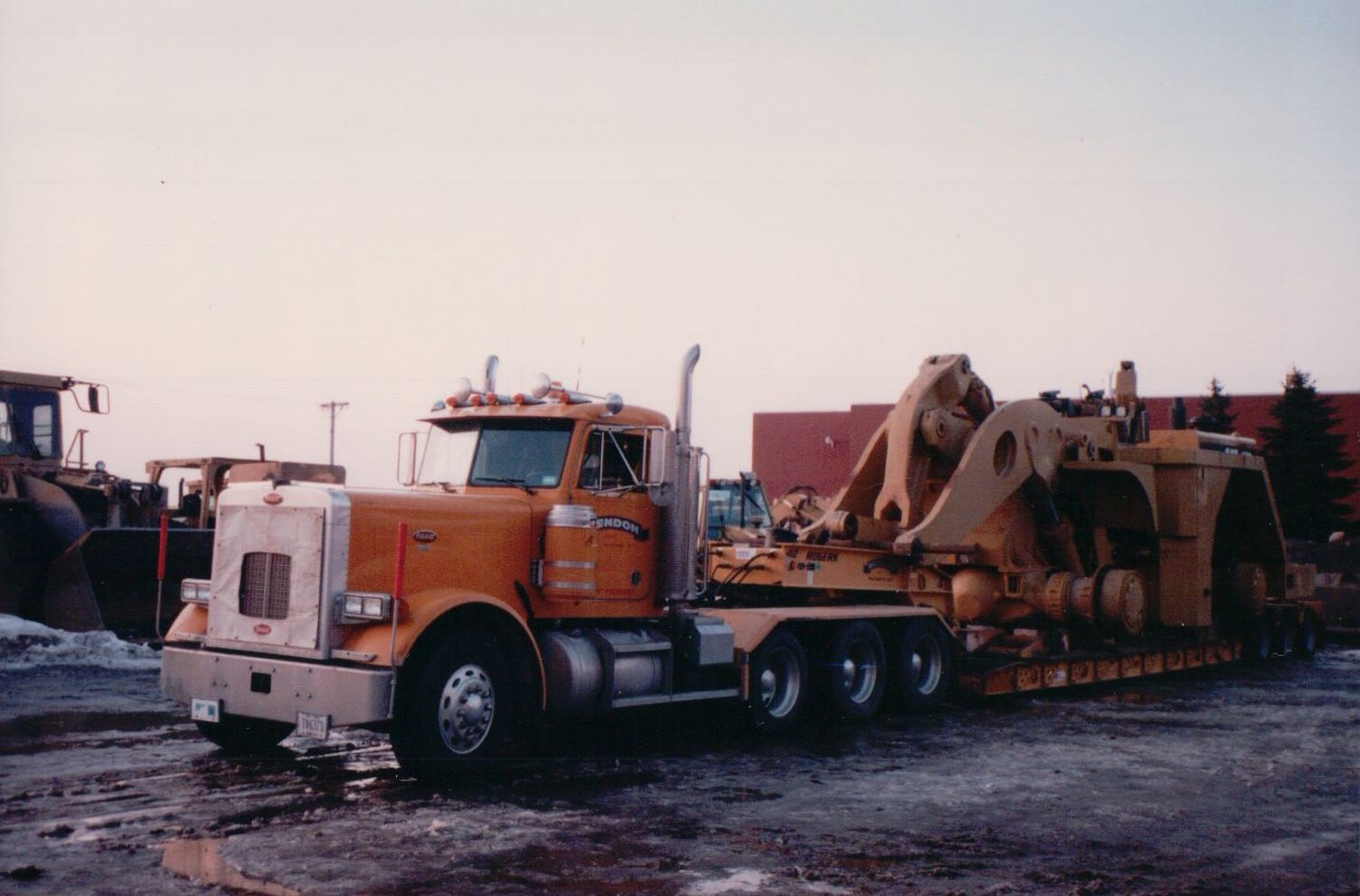 Peterbilt hauling a heavy machinery component at dusk