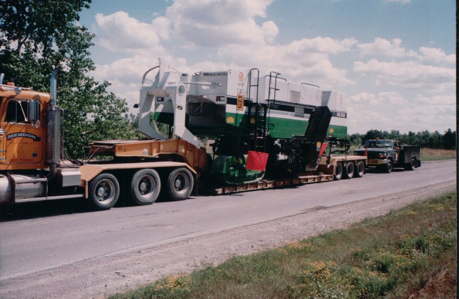 Mack truck hauling a green CMI paver